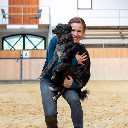 Ildikó trägt ihrer Hündin Csipke auf dem Arm und die beiden zeigen ihre Freude.