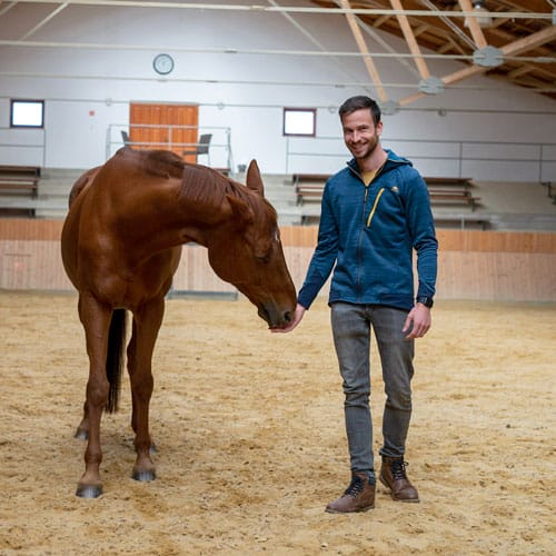 Barnabas, ein junger Mann im Coaching mit Stute Ligah, die an seiner Hand schnüffelt. Darüber freut er sich.